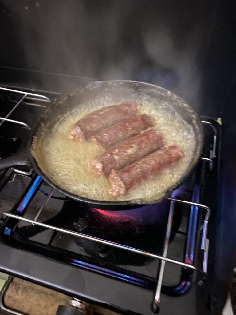 Deer sausage cooking in a frying pan on a camp stove