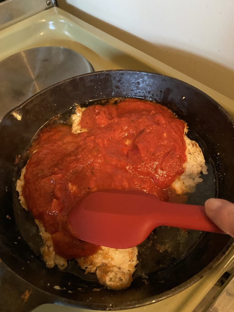 Spreading marinara sauce over the chicken