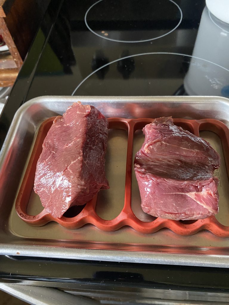 Two six-ounce grass fed sirloin steaks on a pan and OXO rack