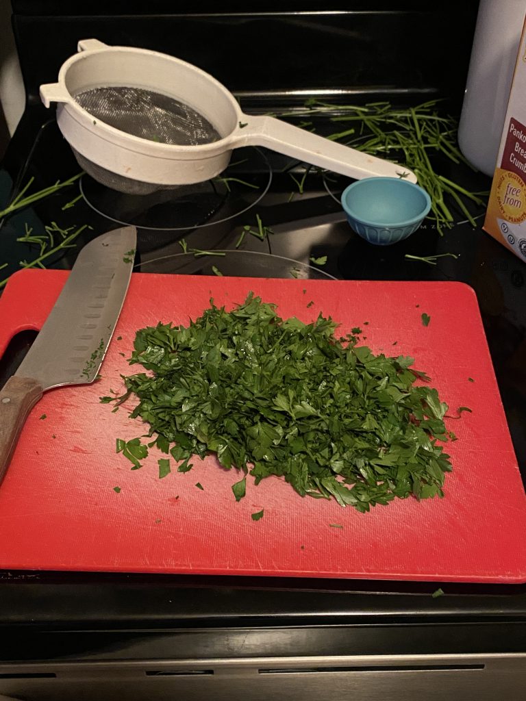 Parsley for crab cakes on cutting board with knife 
