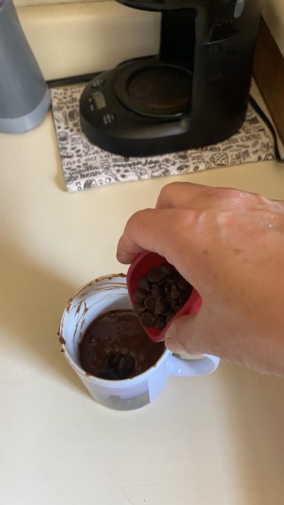Chocolate chips stirred into the chocolate cake in a cup